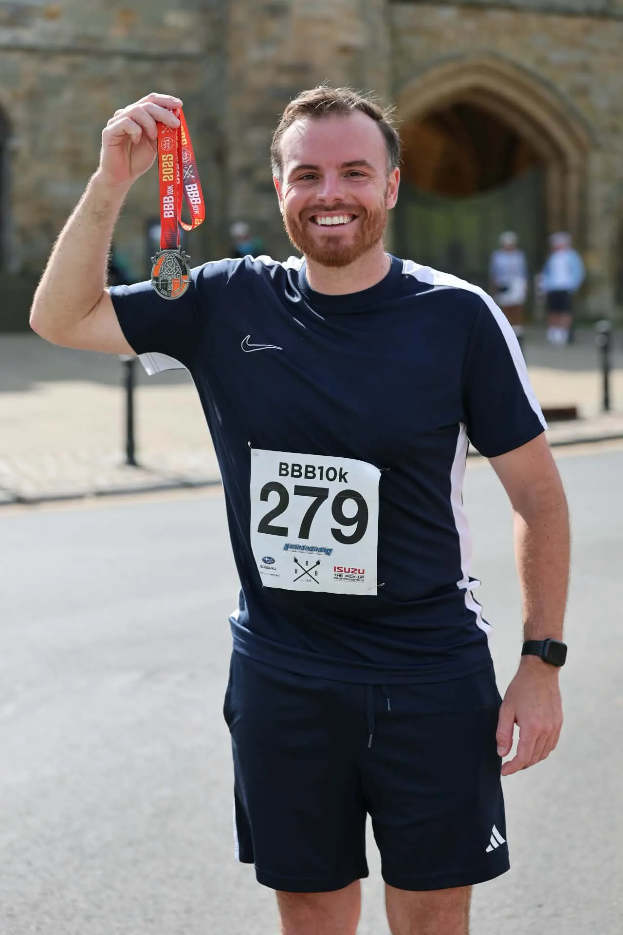 A runner proudly holding up his BBB10k finisher's medal in front of Battle Abbey